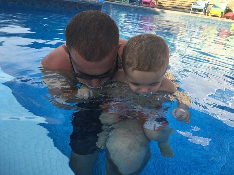 Father and son in pool blowing bubbles
